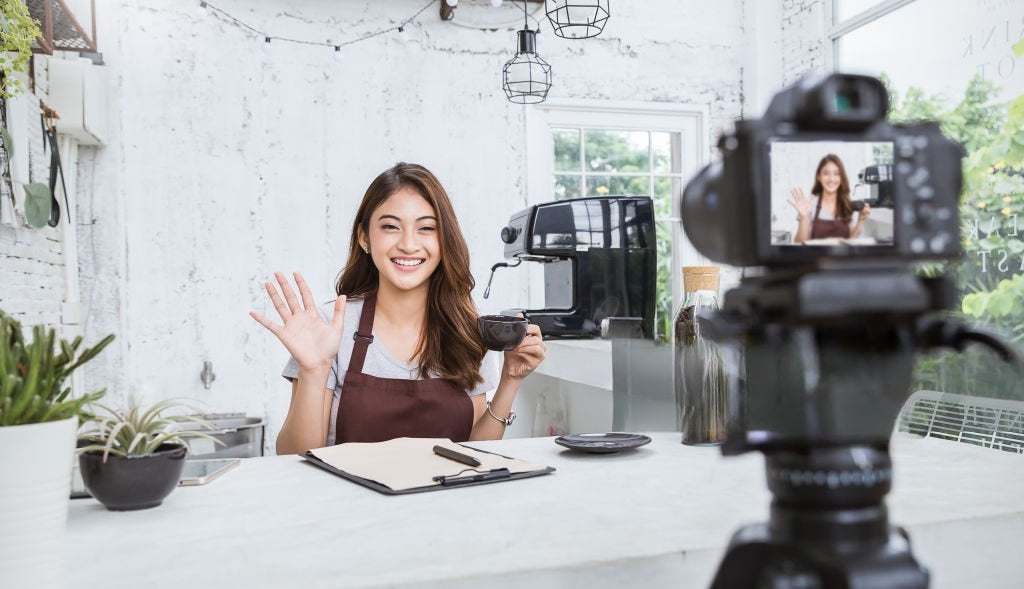 Woman smiling and waving while recording a podcast